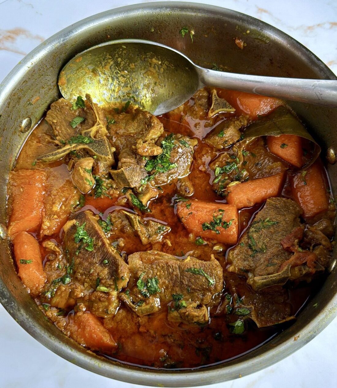 Lamb chops curry in a saucepan with carrots and a spoon