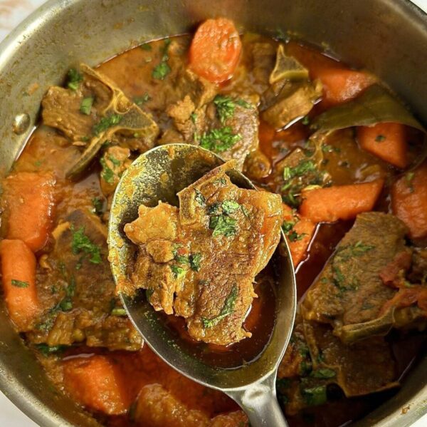 Lamb curry in sauce pan and spoon holding one lamb chop