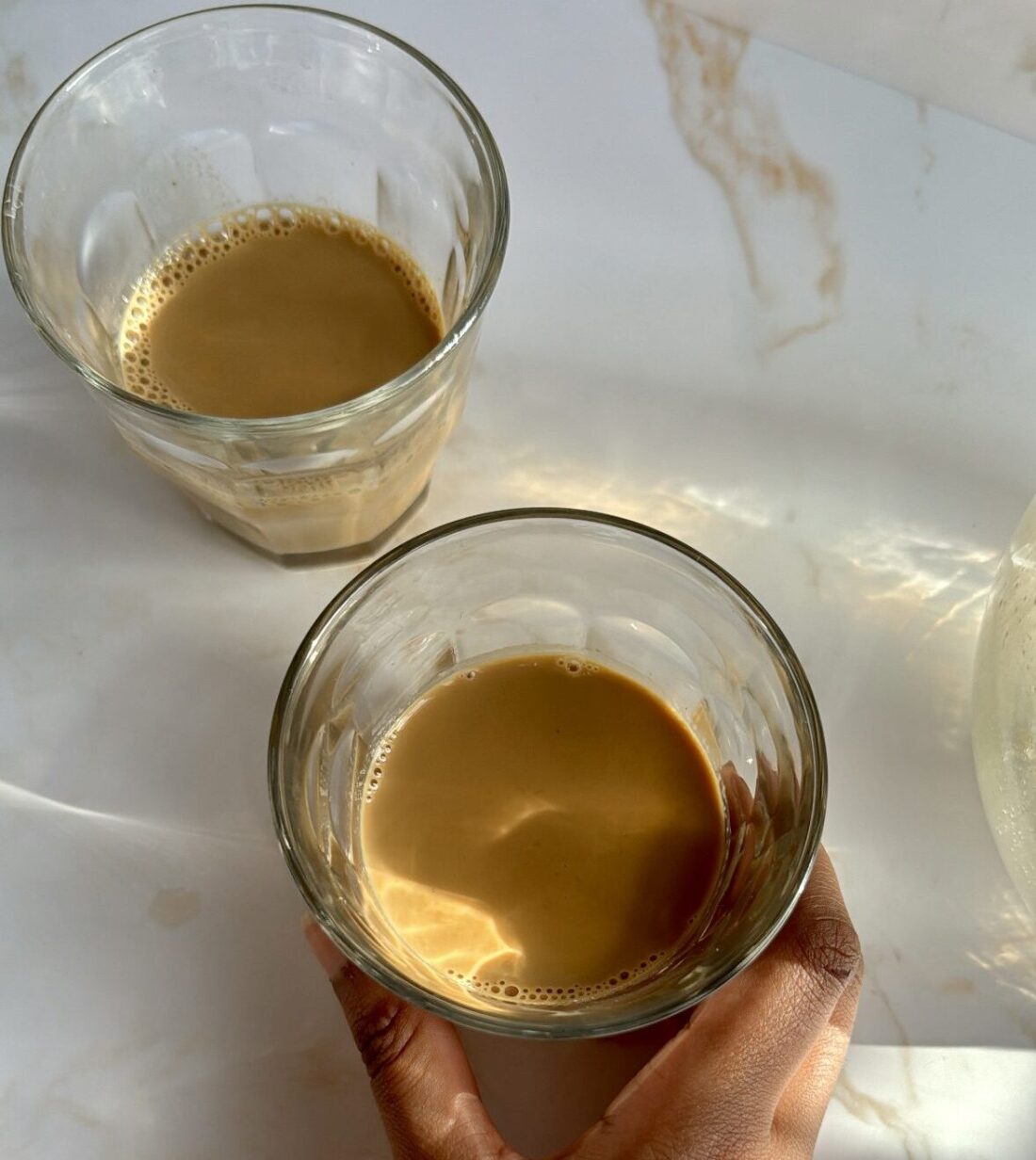 two glasses of karak chai and hand holding chai