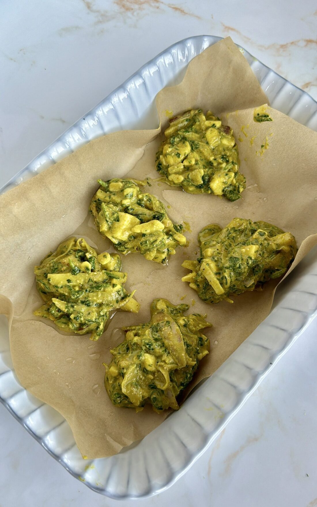 Uncooked pakora balls in white baking tray