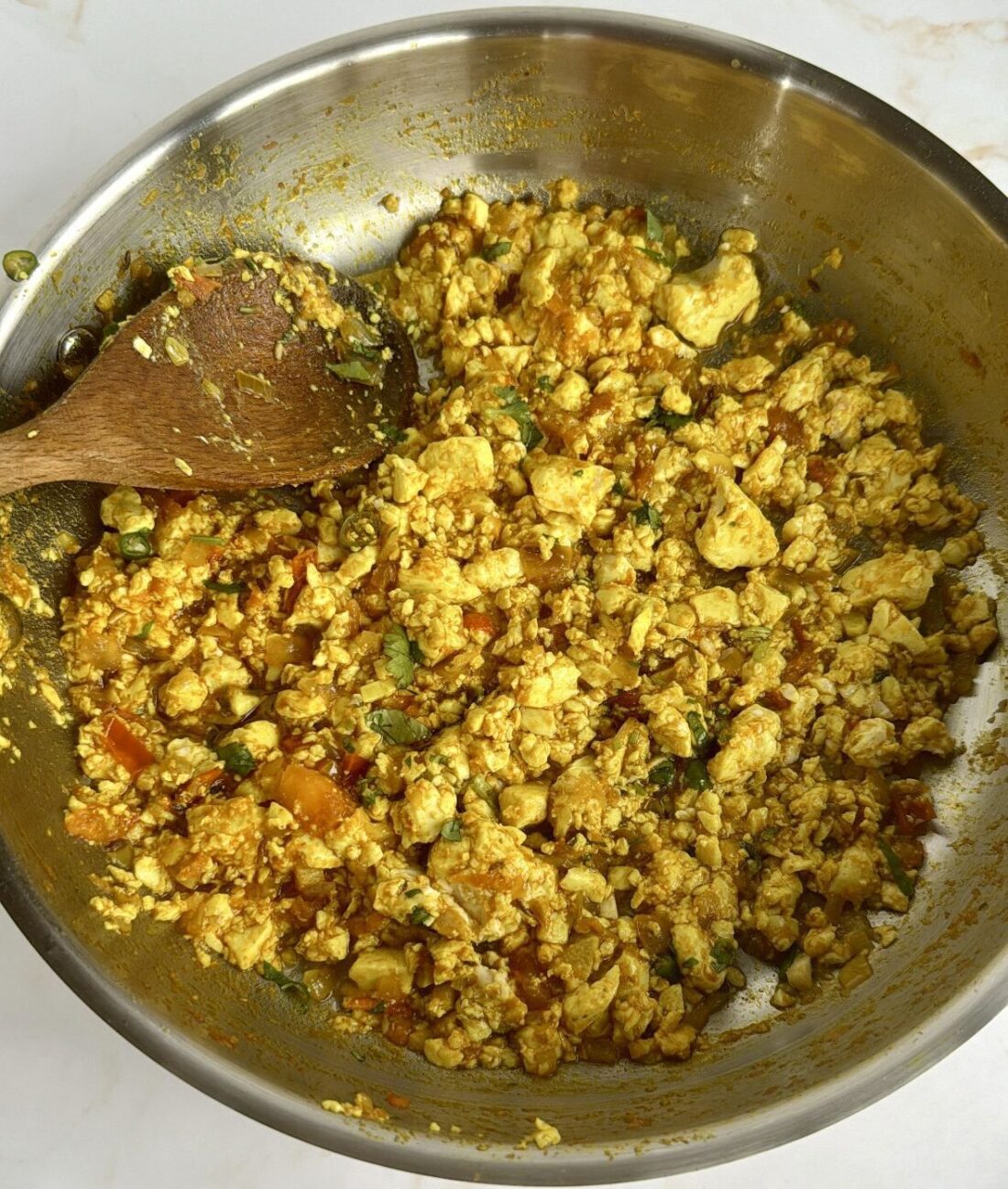 Tofu scramble in a stainless steel pan with a wooden spoon