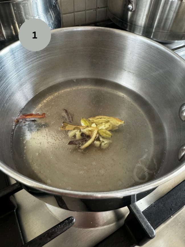 cardamom, cinnamon and other spices infused in water in a saucepan being heated up