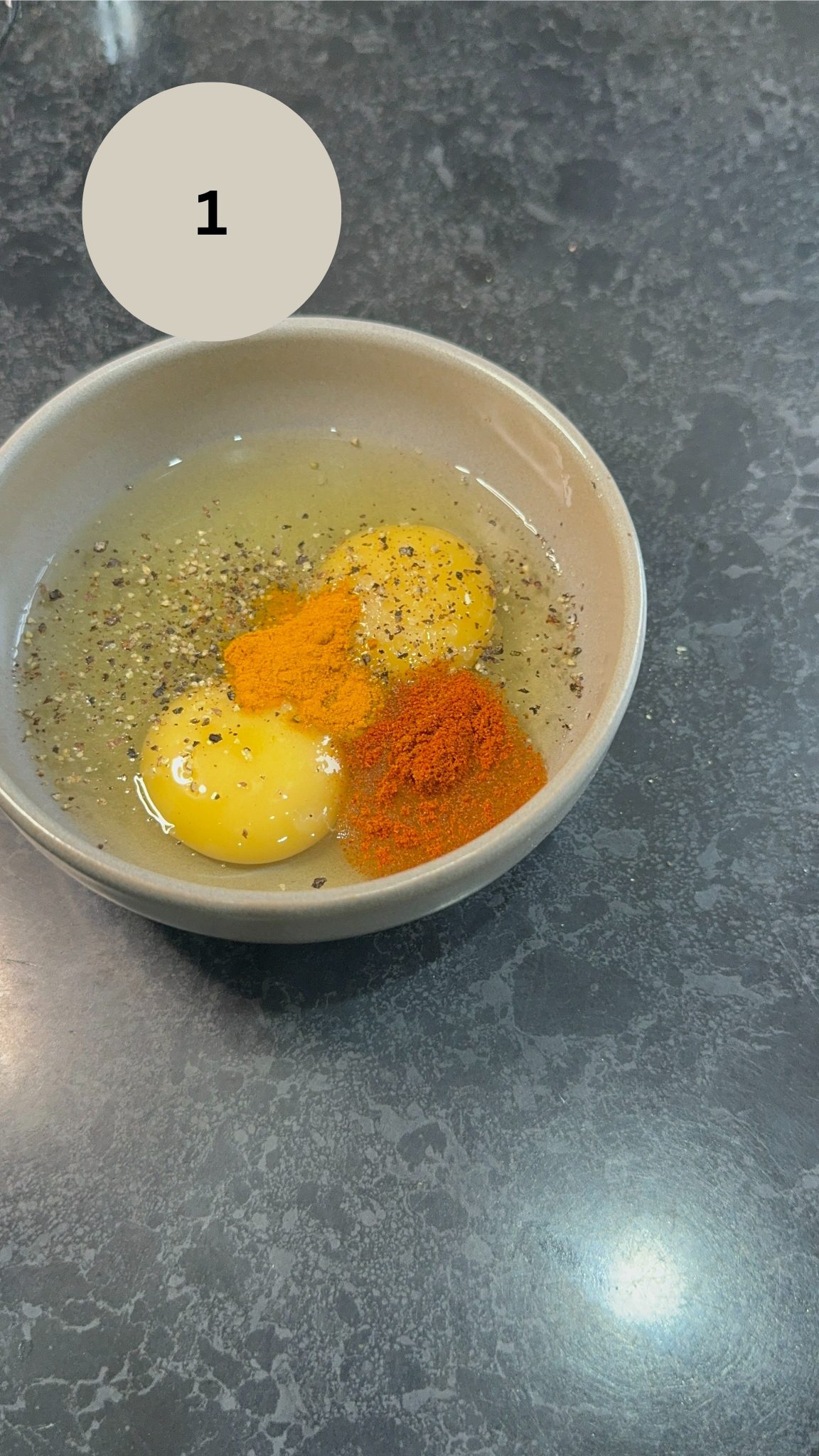 two cracked eggs in a bowl with turmeric, chilli powder and cracked black pepper