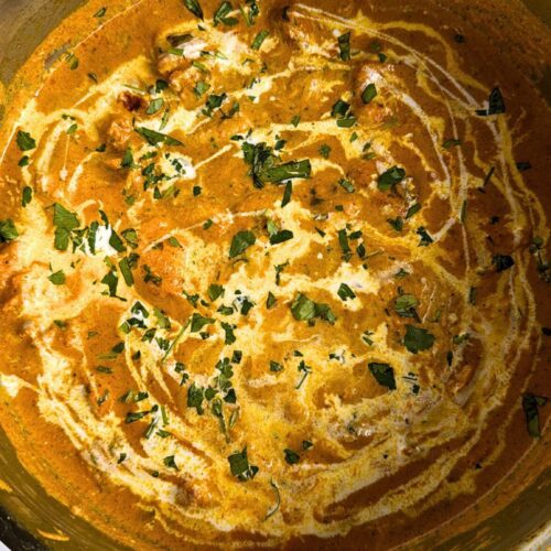 Butter Chicken in creamy yellow sauce, garnished with cream and coriander