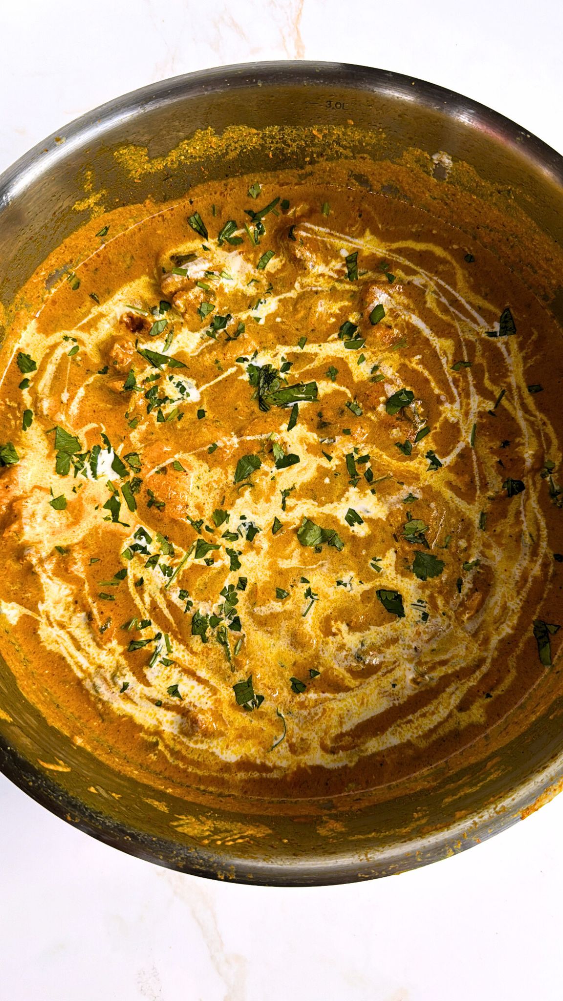 Butter Chicken in creamy yellow sauce, garnished with cream and coriander