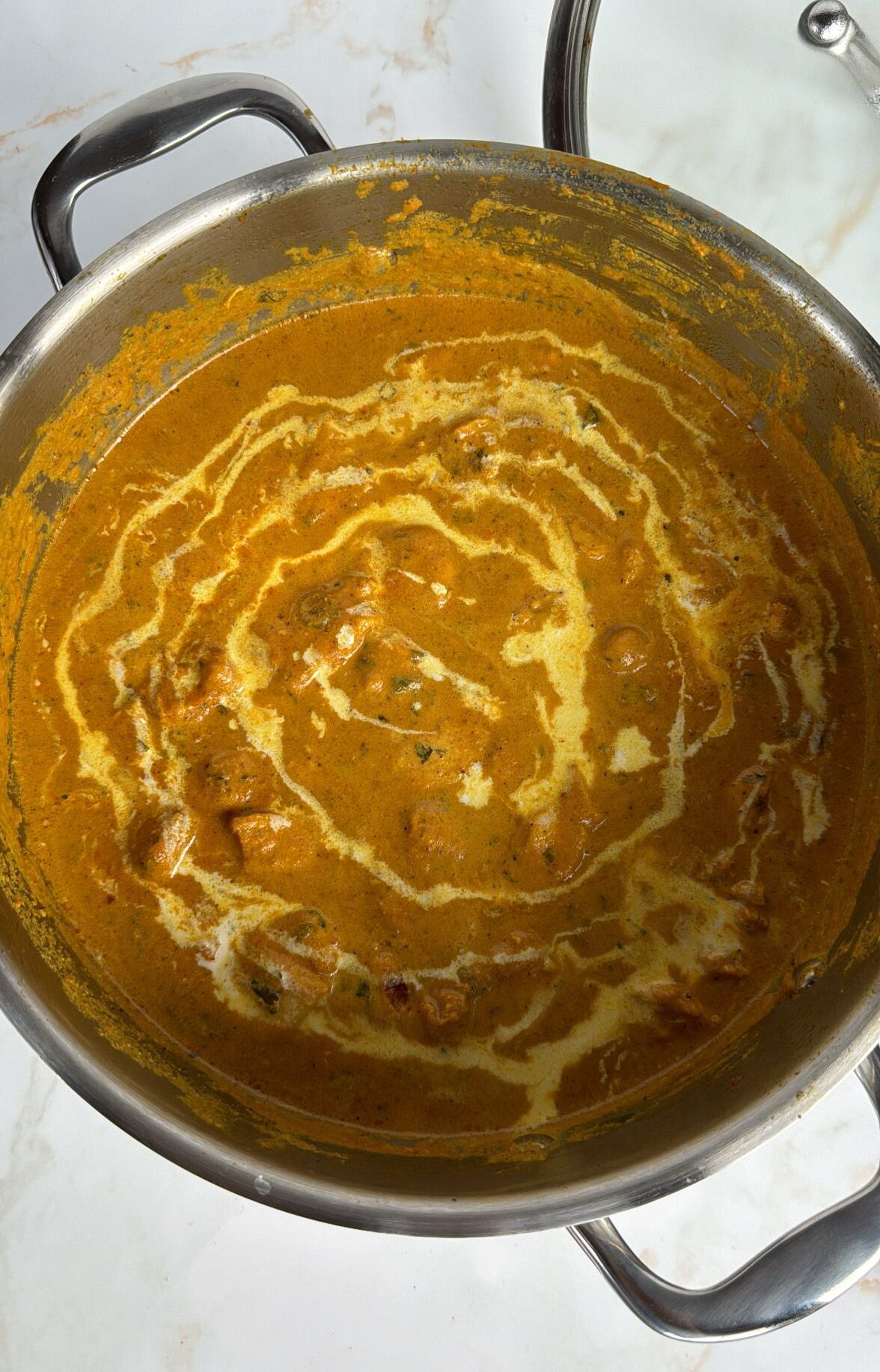 butter chicken curry in a pan with cream drizzled on top