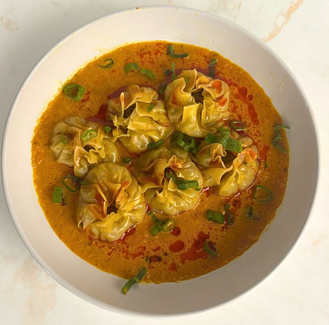 momos in tomato achar sauce toppped off with chilli oil and spring onions