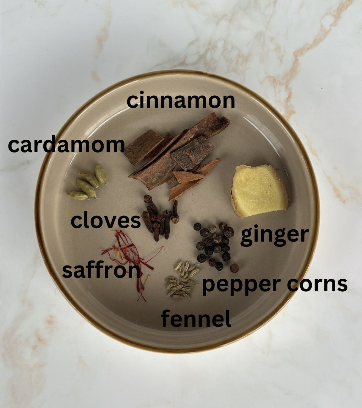 masala chai ingredients laid out: cinnamon, ginger, peppercorns, fennel, cloves, saffron, cardamom