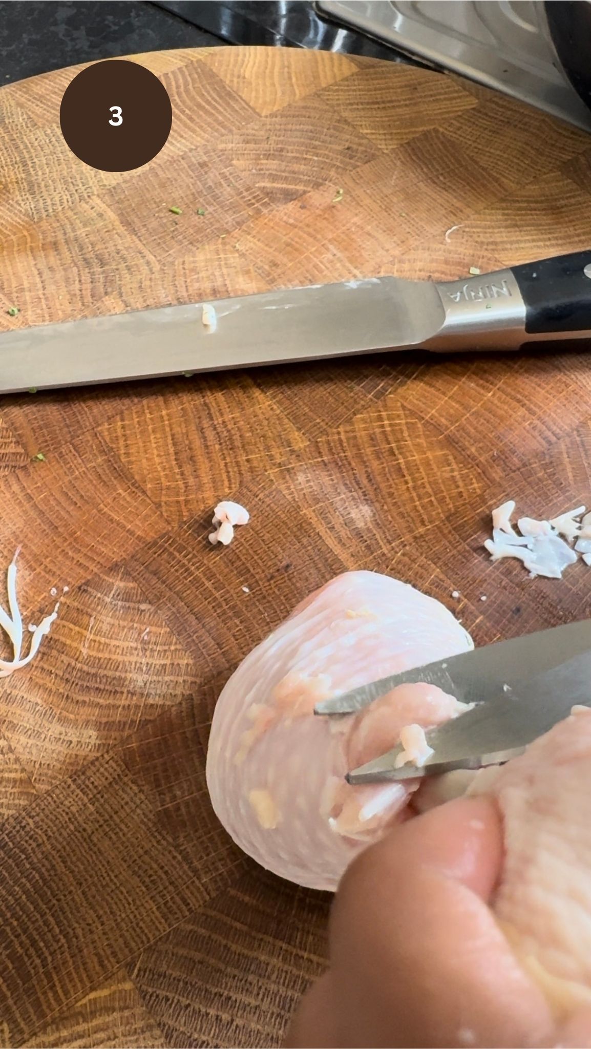 chicken drumstick turned upside down (meat side), knife cutting out excess meat.