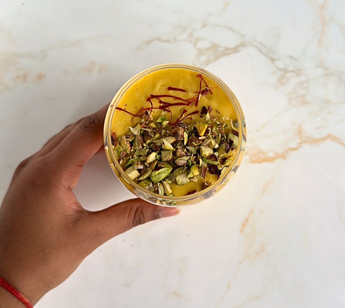 Hand holding the mango lassi in glass.