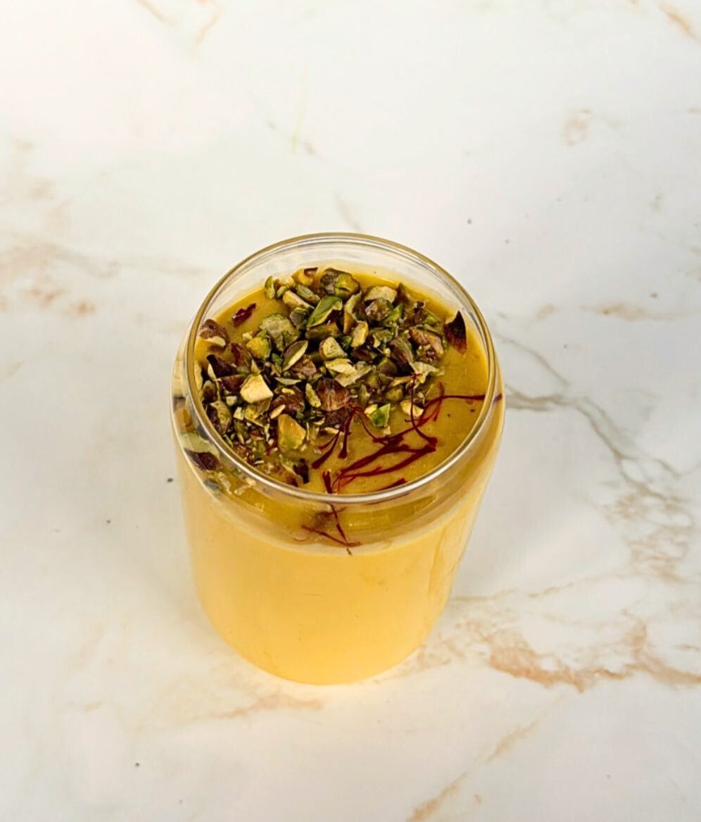 Mango lassi topped with pistachio and saffron in a glass