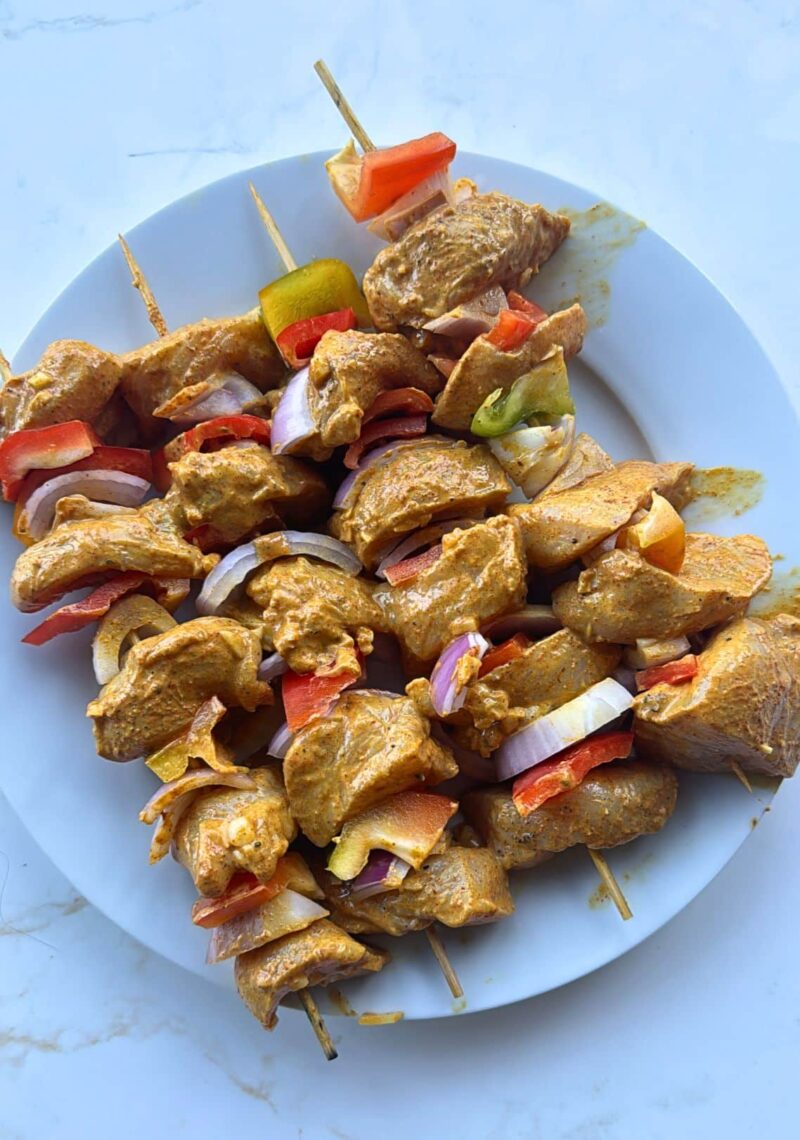 four raw chicken tikka skewers on plate