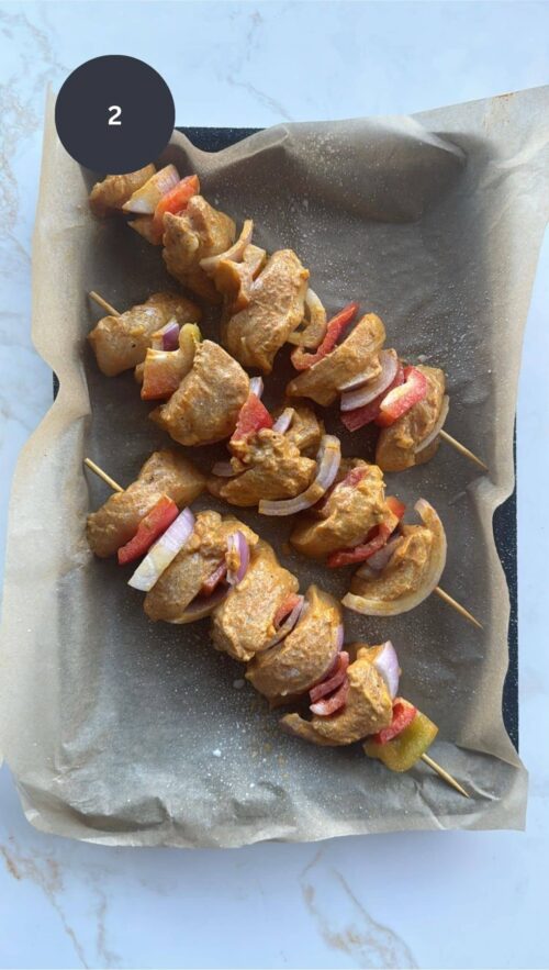 raw chicken tikka skewered on baking tray