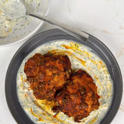 two tandoori chicken thighs on a plate resting on yoghurt dill sauce