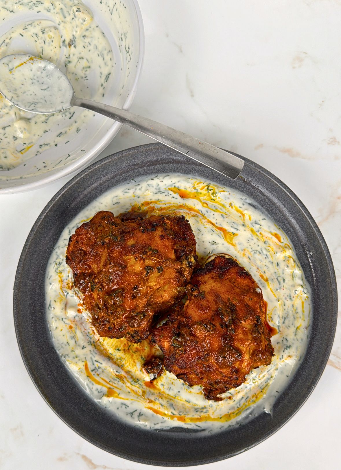 two tandoori chicken thighs on a plate resting on yoghurt dill sauce